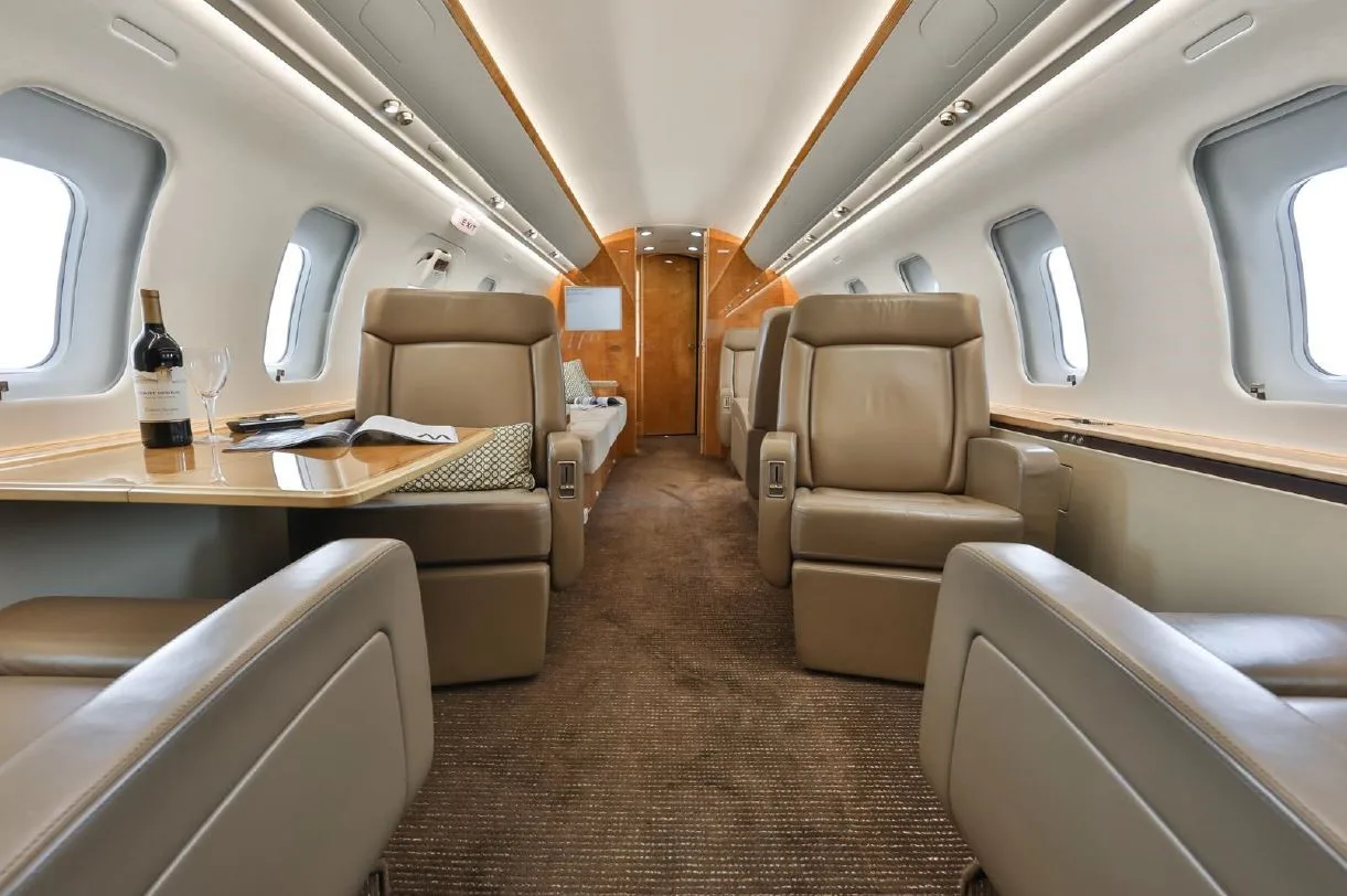 A view of the private jet's interior cabin with beige seats, a table set with wine, and elegant wood finishes.