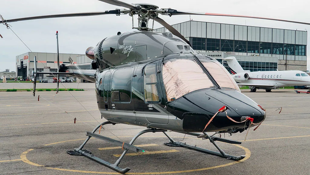 A front-quarter view of a black and silver Bell 427 helicopter with sunshades, parked on an airfield.