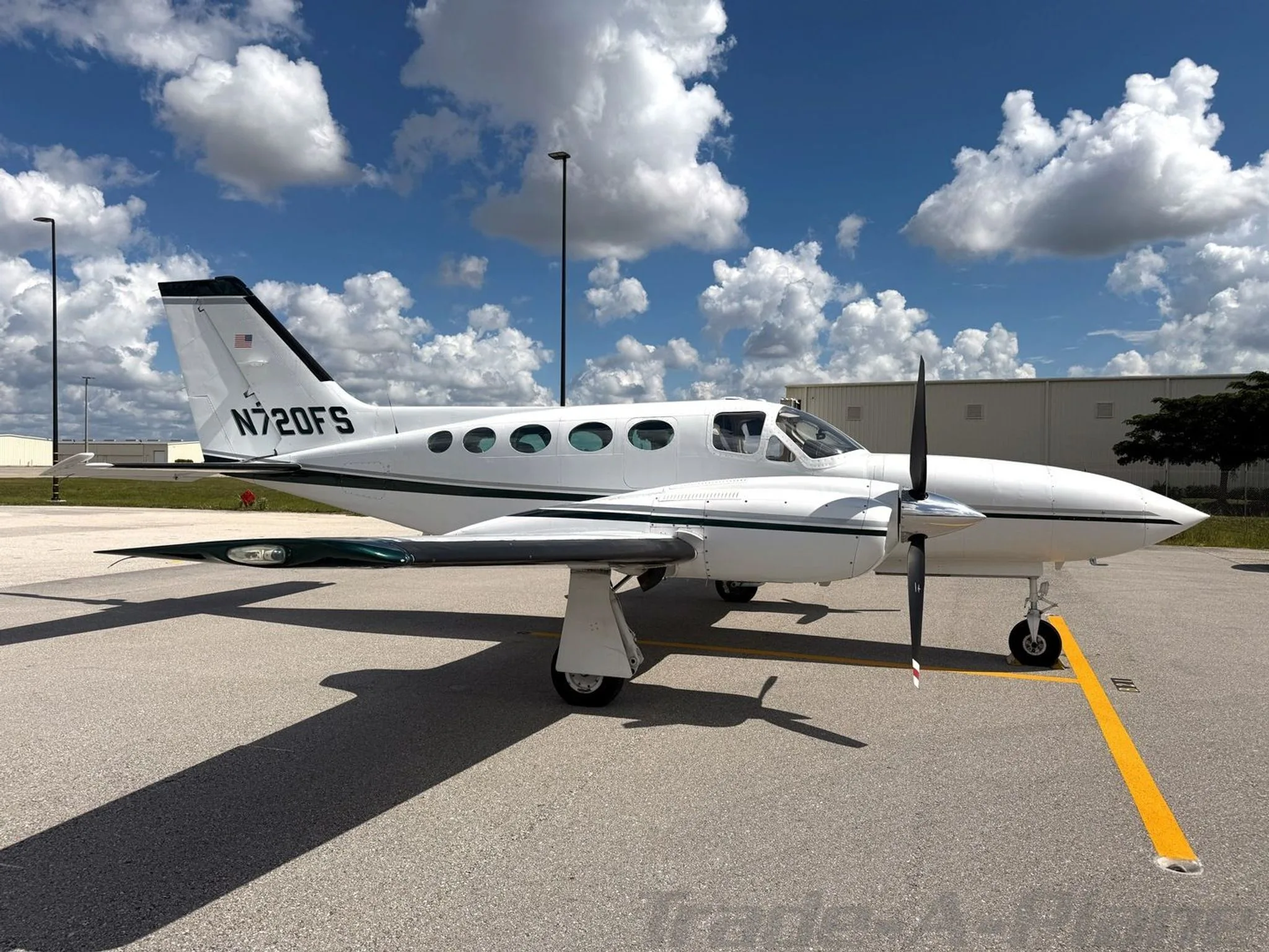 A white Cessna 414 Chancellor aircraft, N720FS, with dark green stripes, parked on an airfield, viewed from the left side.