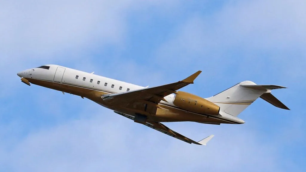 A white and gold Bombardier Global Express business jet climbing against a blue sky.
