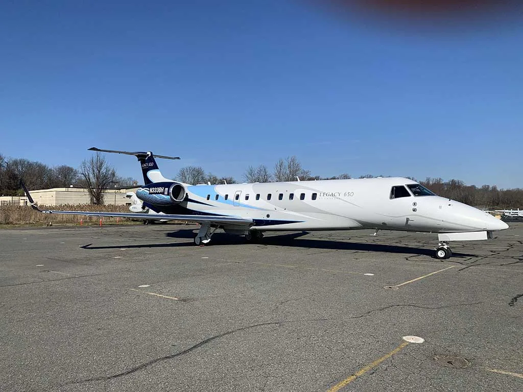 A white and blue Embraer Legacy 650 (N333BH) parked on an asphalt tarmac under a clear blue sky.