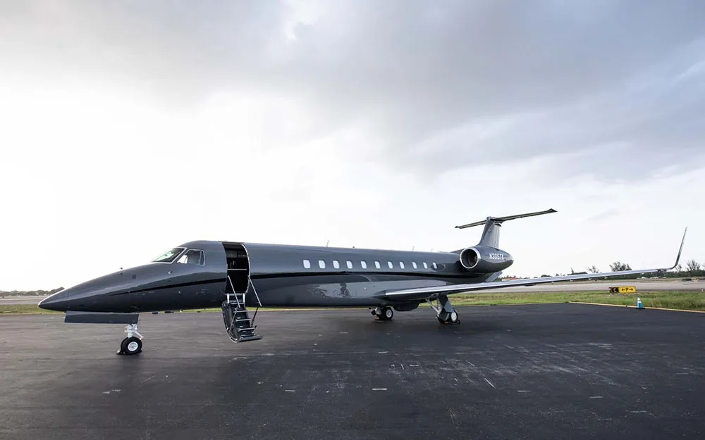 A dark grey Embraer Legacy 600 business jet (N305TK) parked on an airfield with its main door open.