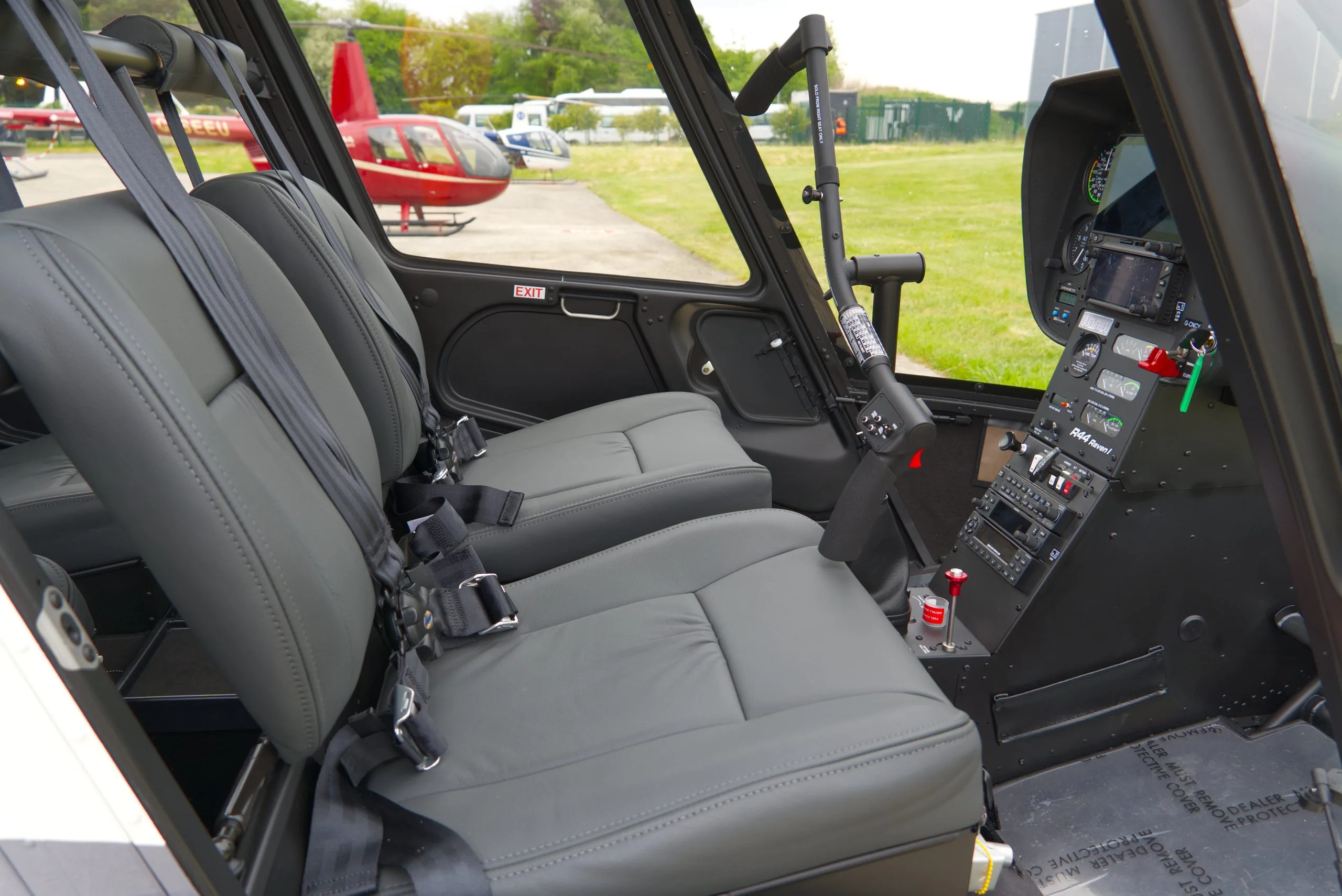 The grey leather seats and partial cockpit of a Robinson R44 helicopter are visible from inside the cabin.