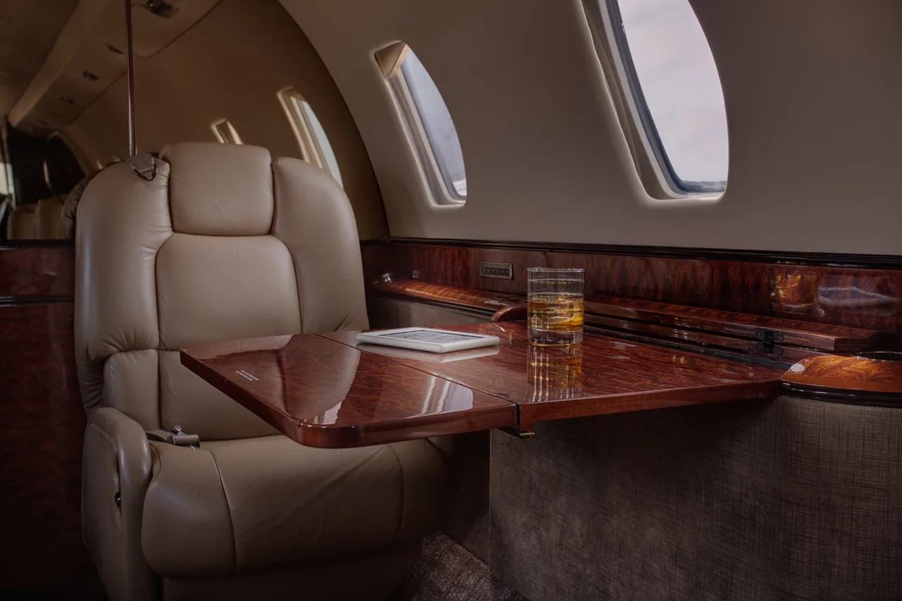 Aircraft interior with leather seat, wood accents, and a table with a drink.