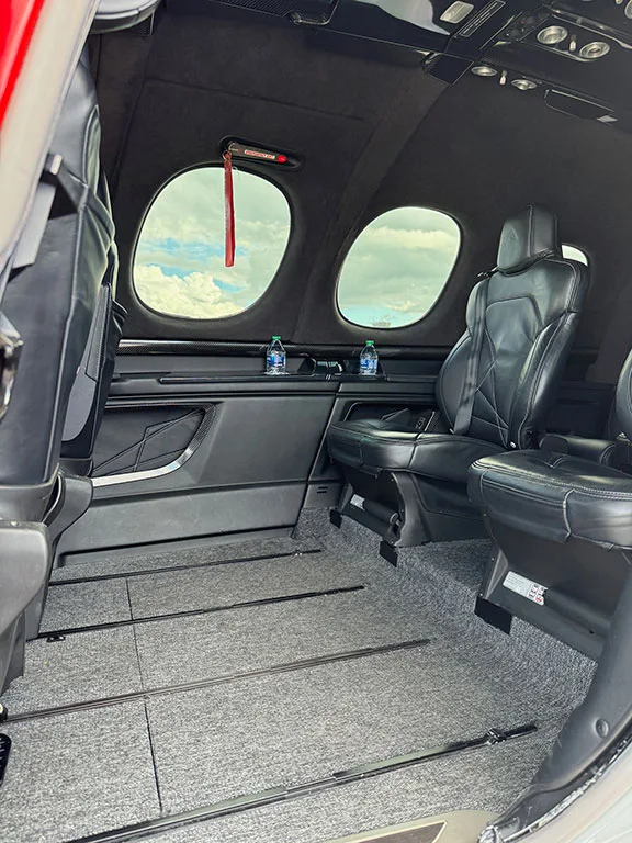 The aircraft cabin interior with black leather seats, grey carpet, and two windows.