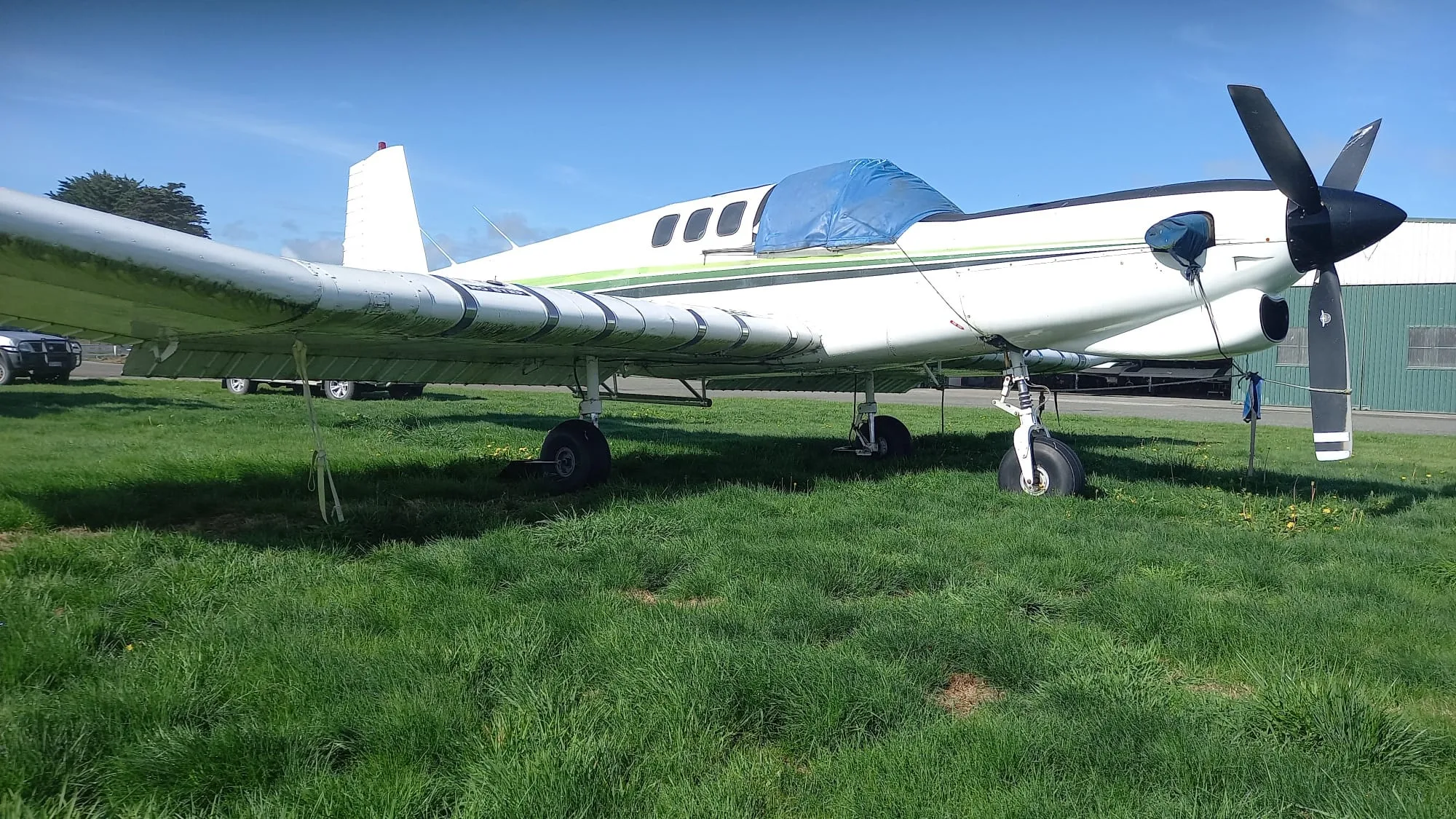 A white single-engine turboprop aircraft with green stripes, parked on a grassy field under a blue sky.