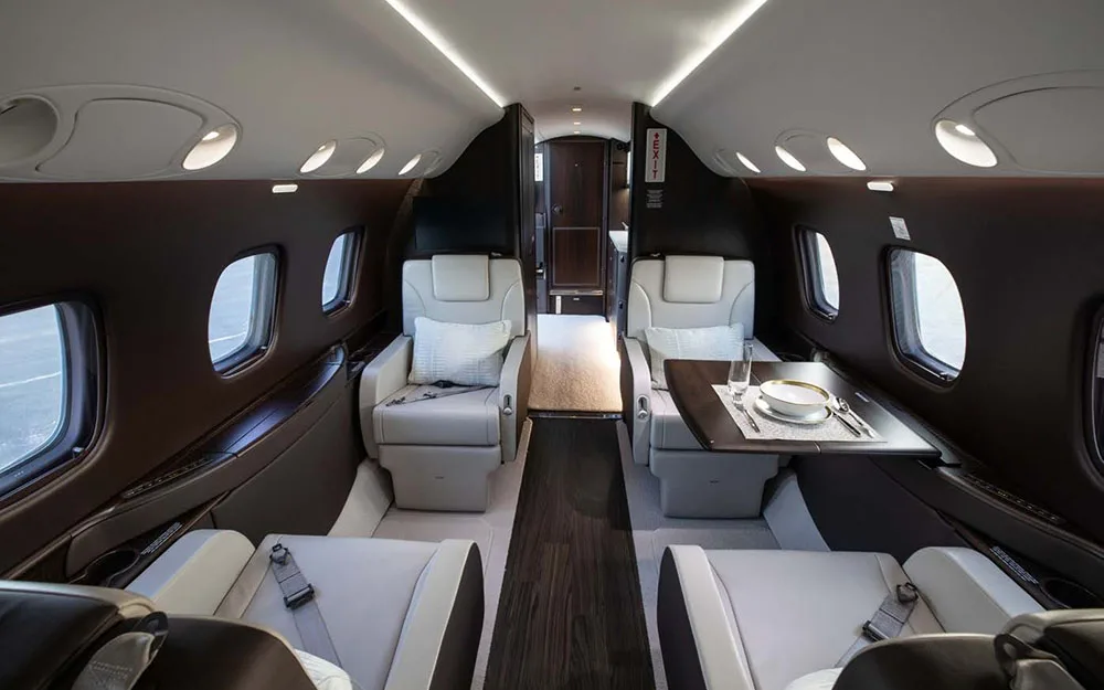 The luxurious interior cabin of a private jet, featuring light-colored seats and a dining table setup.