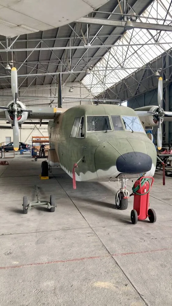 A front view of a camouflage military transport aircraft with propellers in a hangar.