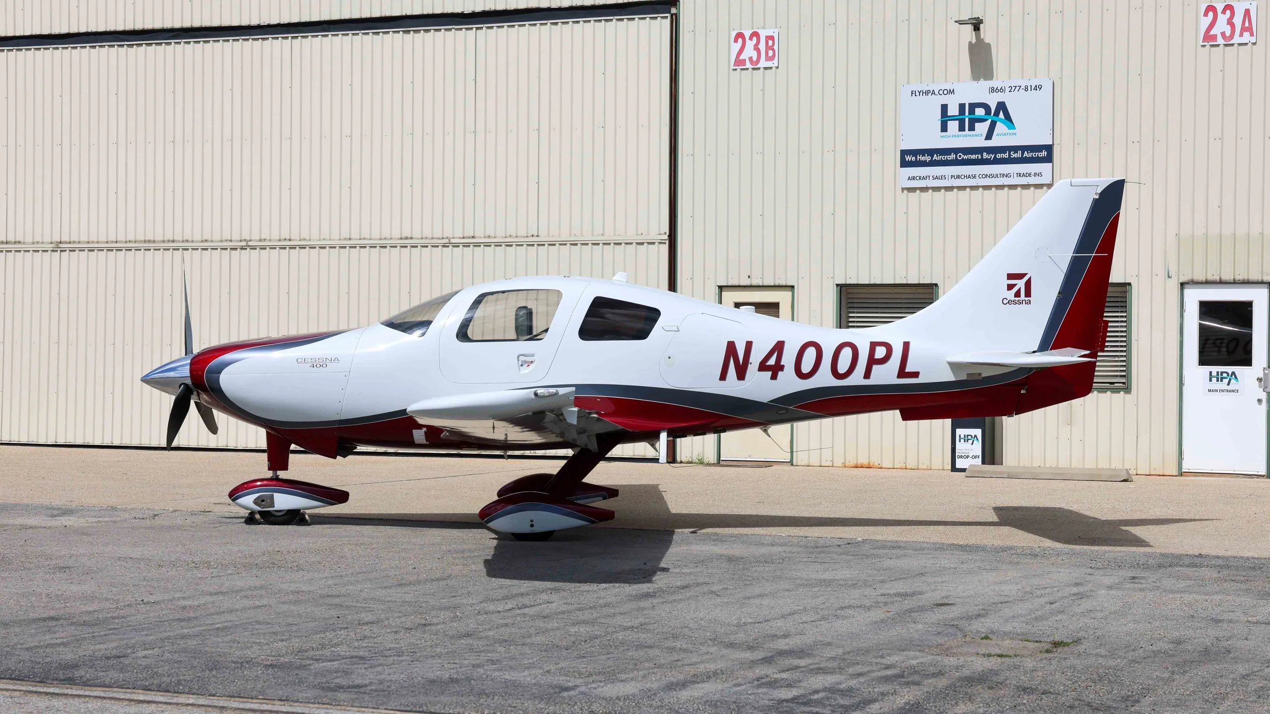 A white and red Cessna 400 aircraft, N400PL, parked in front of hangars.