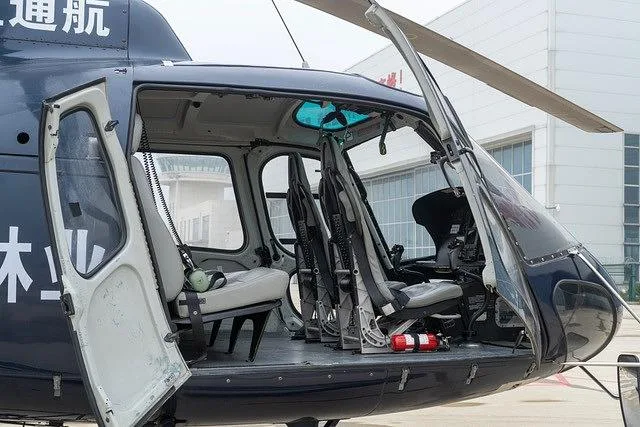 The dark blue helicopter's doors are open, revealing the light gray passenger seats and a partial view of the cockpit.