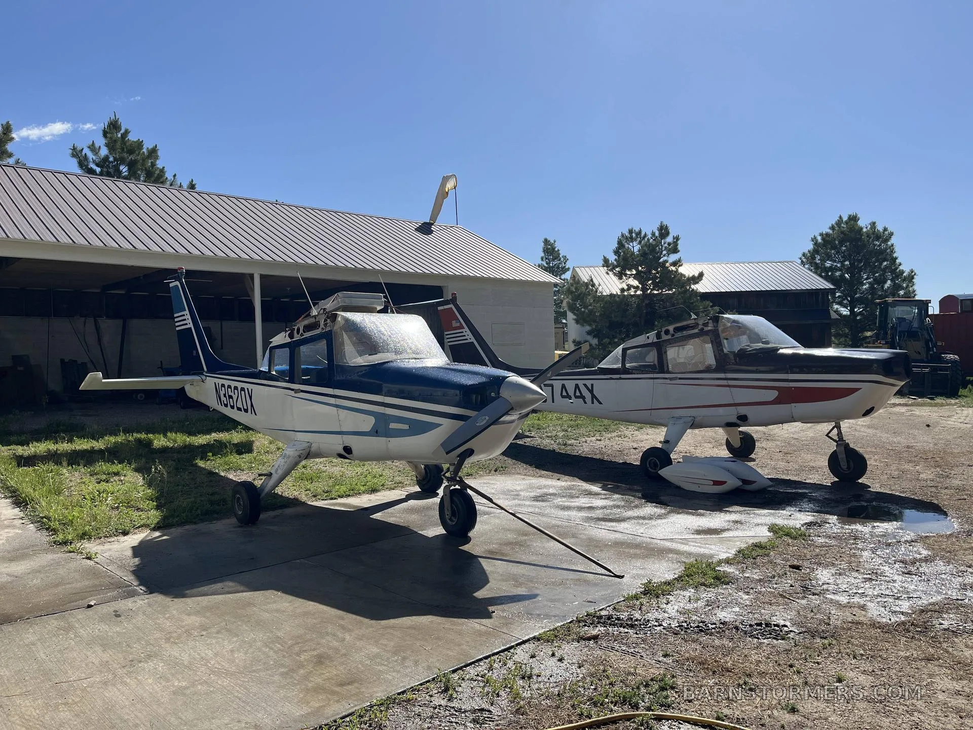 Two single-engine propeller aircraft, one blue and white (N3620X) and one brown and white (N3744X), parked on a concrete pad in front of a hangar.