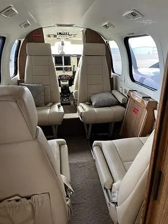 The aircraft's interior cabin features light-colored leather seats and a view looking forward into the cockpit.