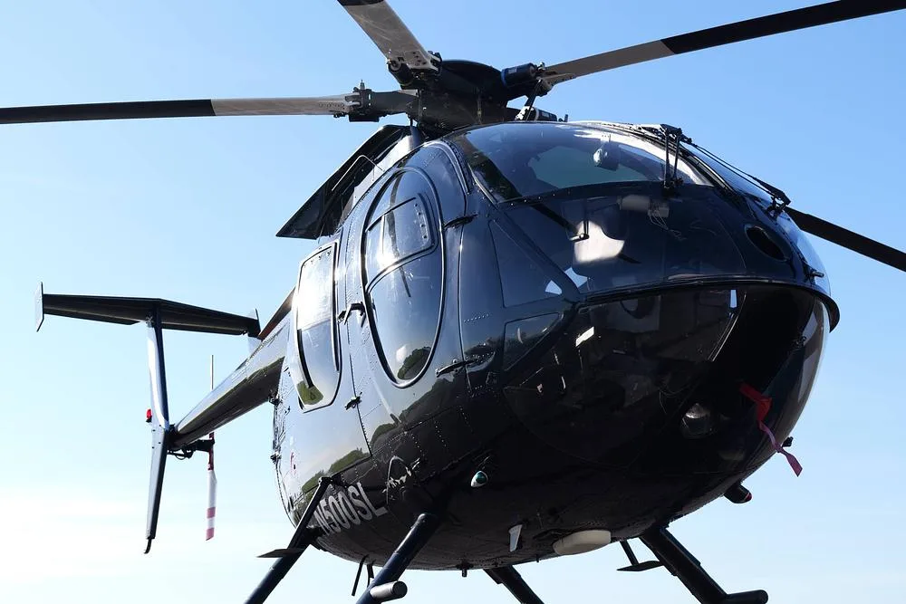 A detailed front-right view of a black MD 500 helicopter (N500SL) on an airfield.