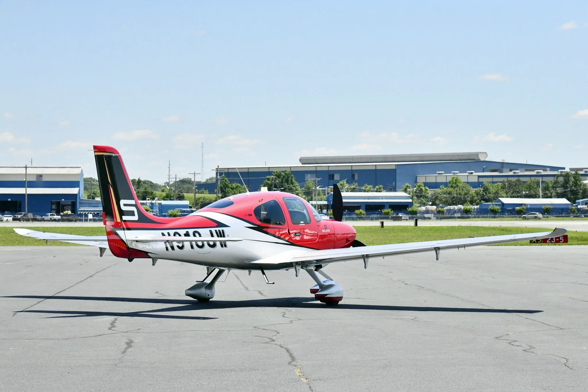 A red and white Cirrus SR22T aircraft with registration N918JW parked on an airfield, viewed from the side.