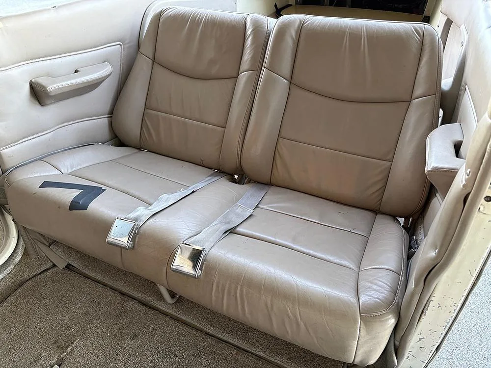 Two tan leather rear passenger seats with seatbelts in a small aircraft cabin.