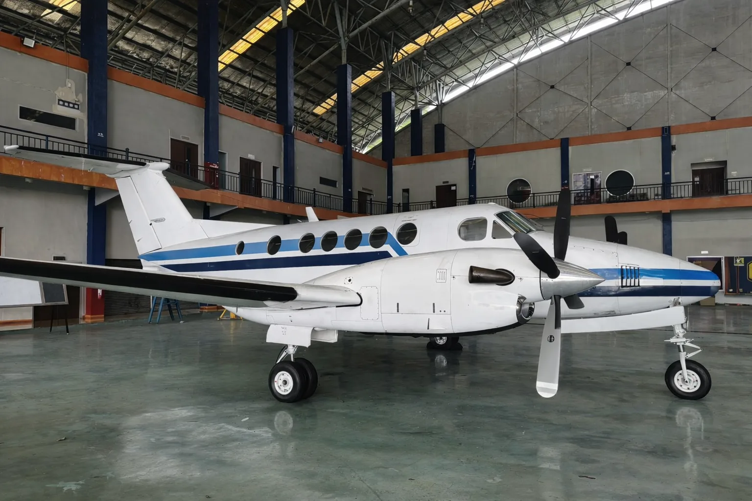 A three-quarter front view of the white and blue twin-turboprop aircraft inside a hangar.