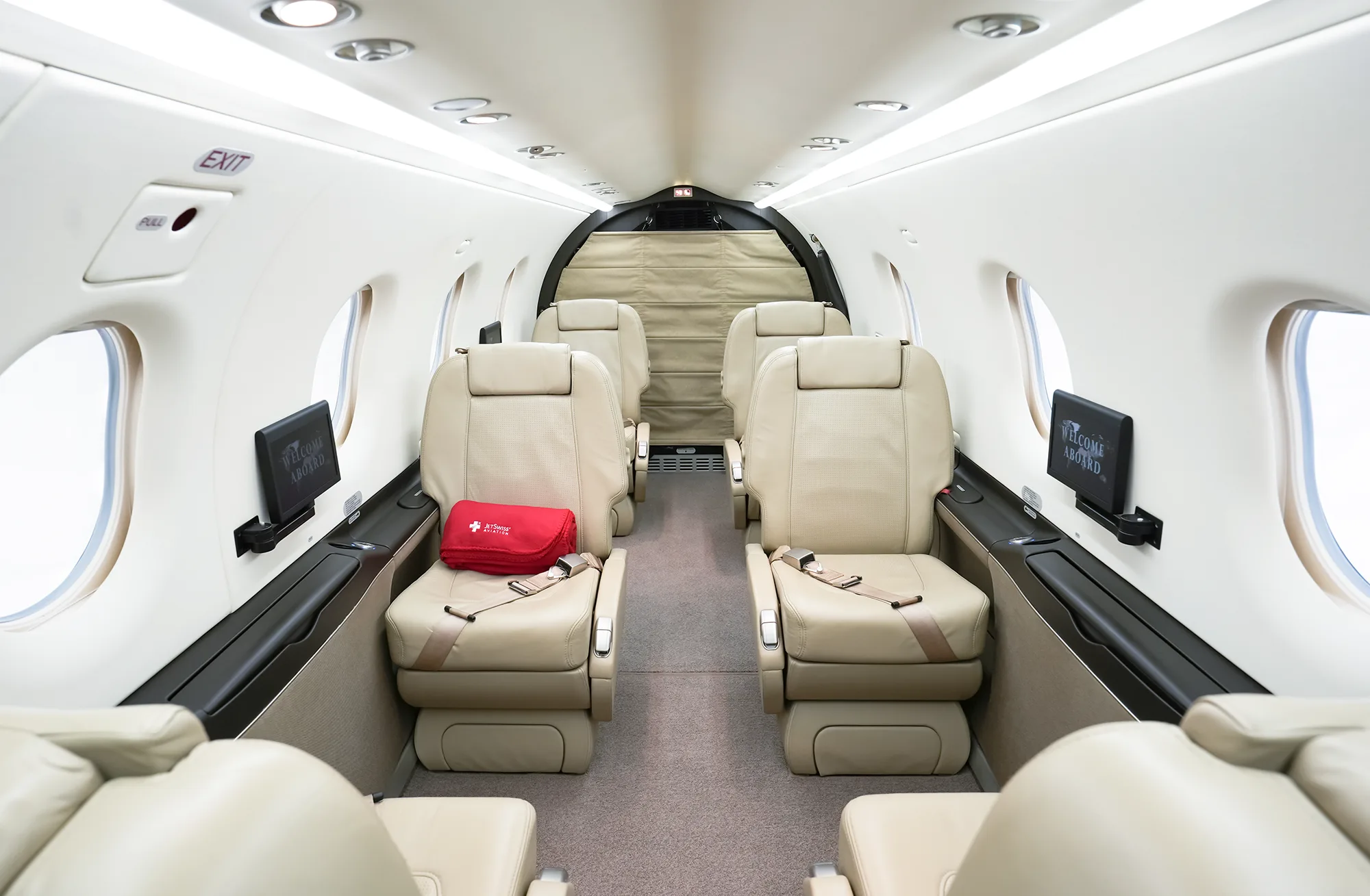 The aircraft cabin interior features beige leather seats arranged in a club configuration, looking towards the rear.