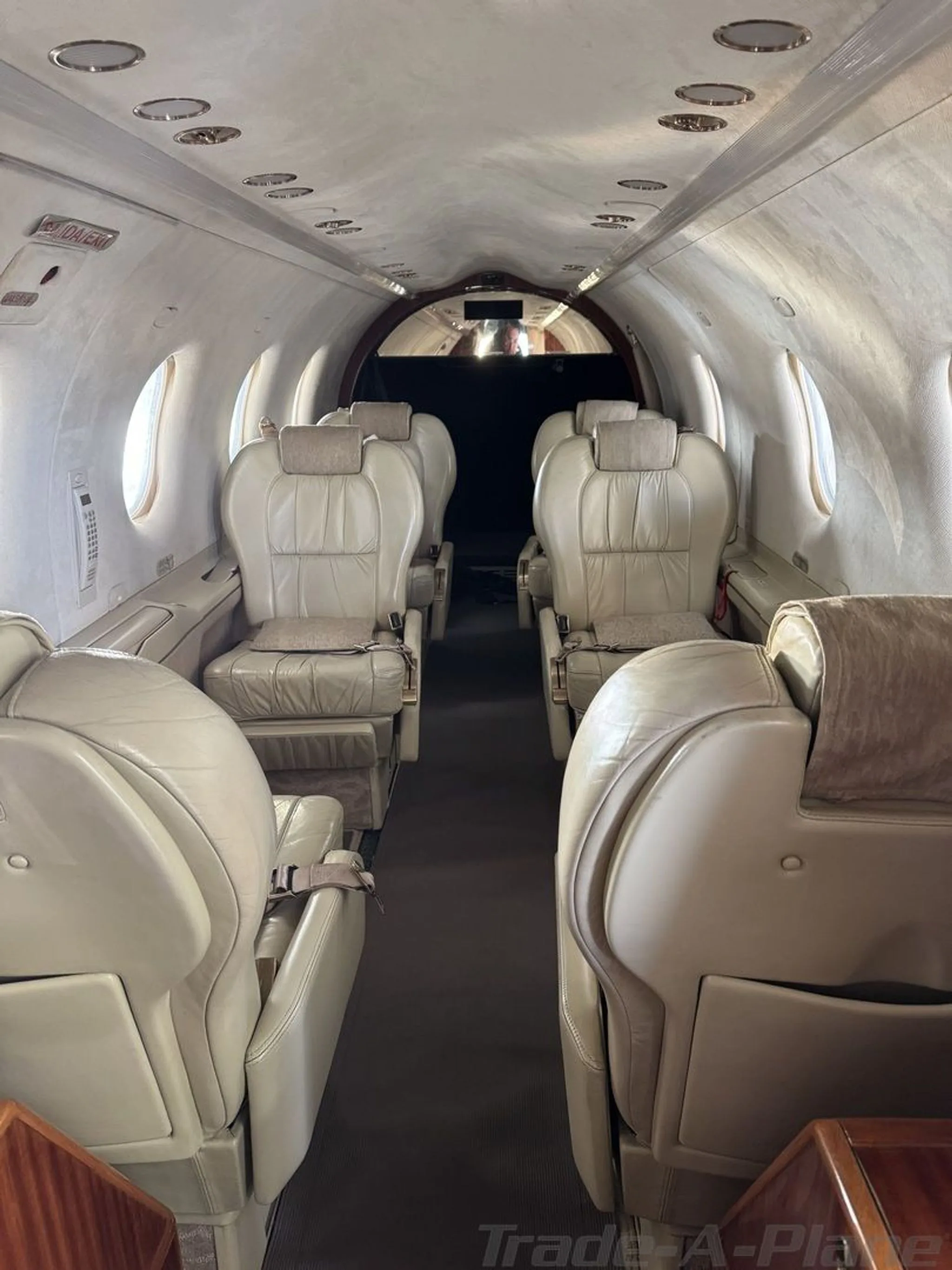 The aircraft cabin interior with light-colored leather seats and a narrow aisle, viewed from the rear.