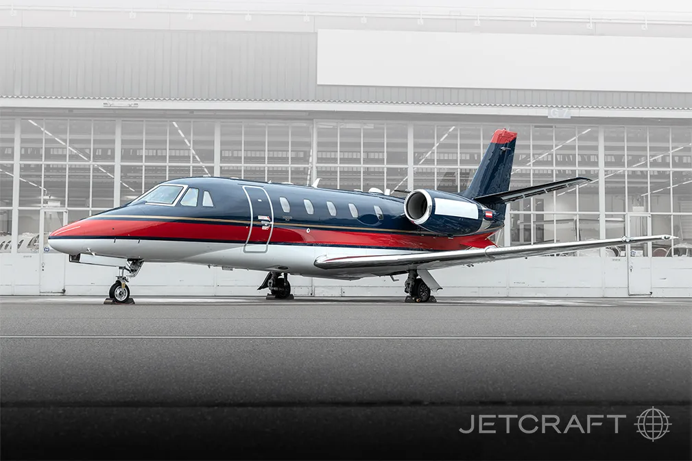 A dark blue, red, and white business jet is parked on an tarmac in front of a hangar.