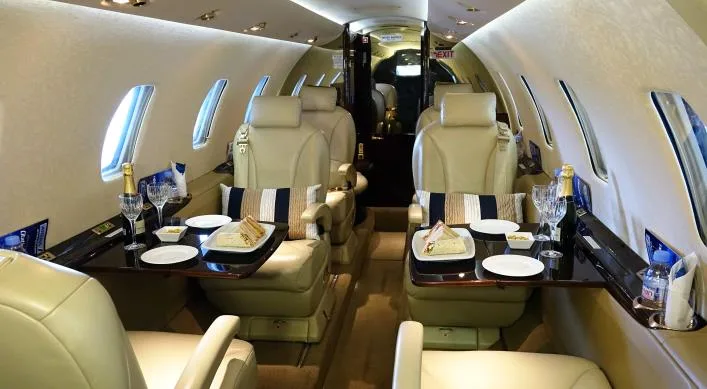 Aircraft interior with leather seats and tables set for a meal.