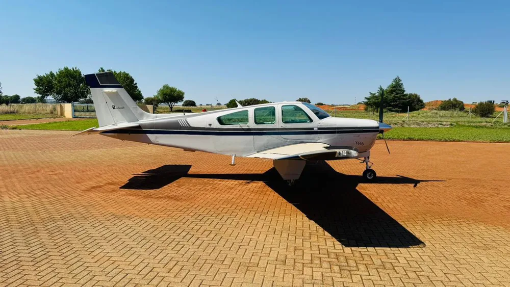 A side view of a white and dark grey single-engine propeller aircraft parked on a brick-paved apron.