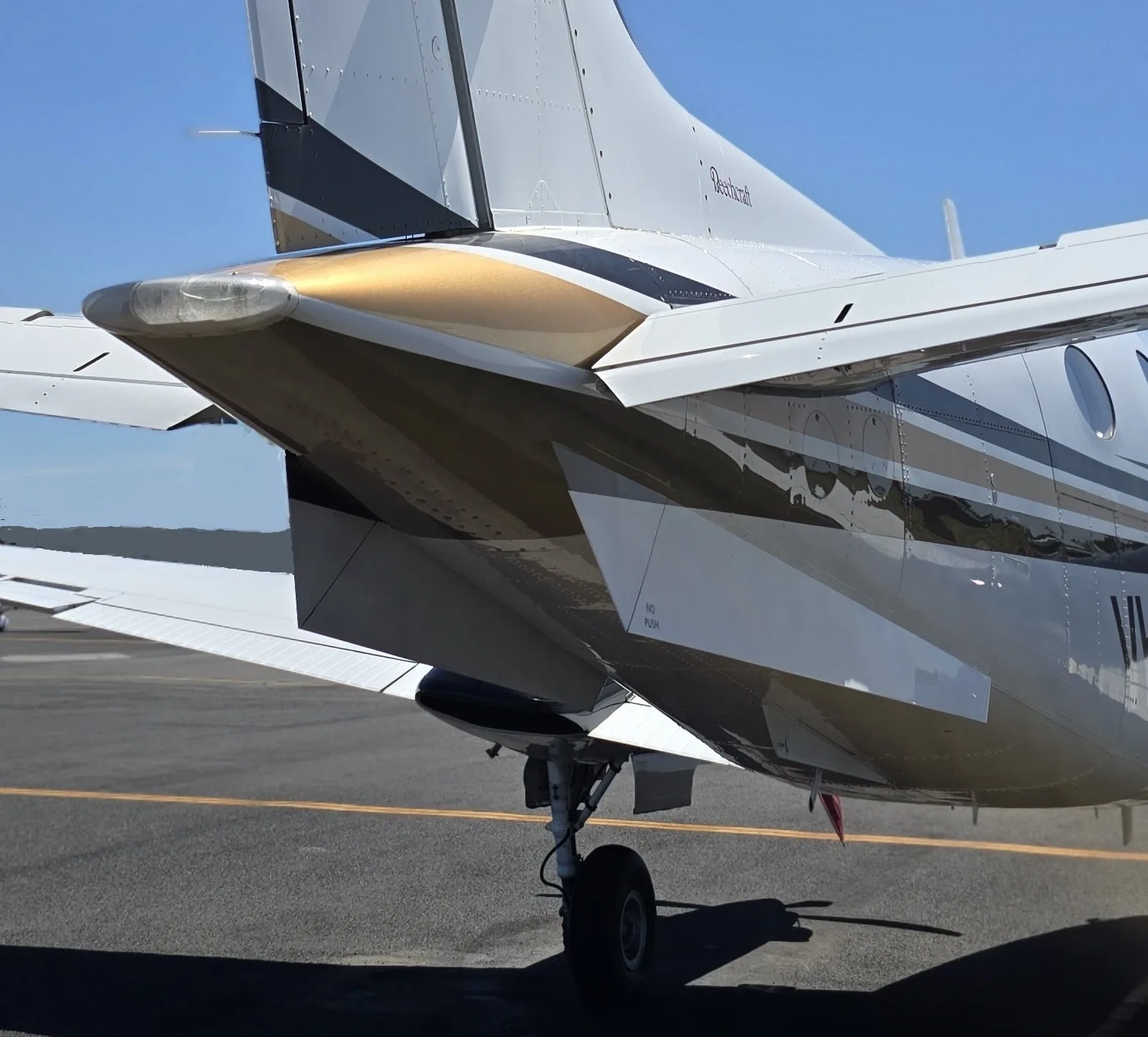 A close-up view of the tail section of a white and gold Beechcraft King Air with a visible registration on the tarmac.