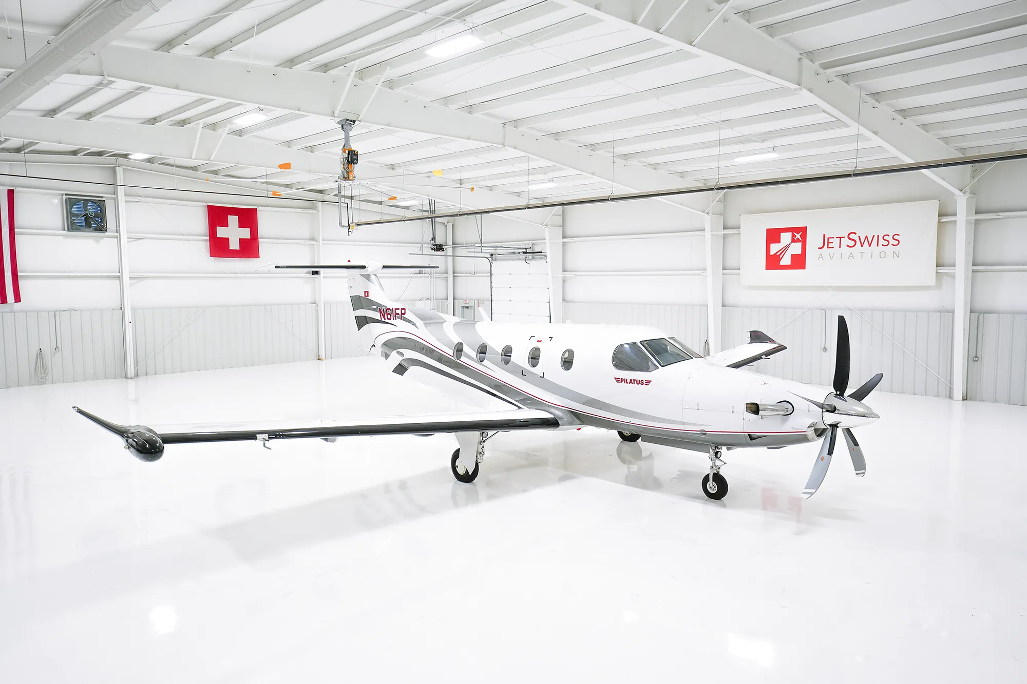 A white Pilatus PC-12 aircraft with registration N61FP is parked inside a brightly lit, white hangar.