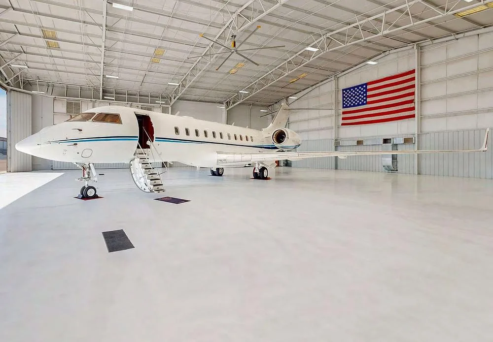A white Bombardier Global Express business jet with blue stripes parked in a hangar with an American flag.
