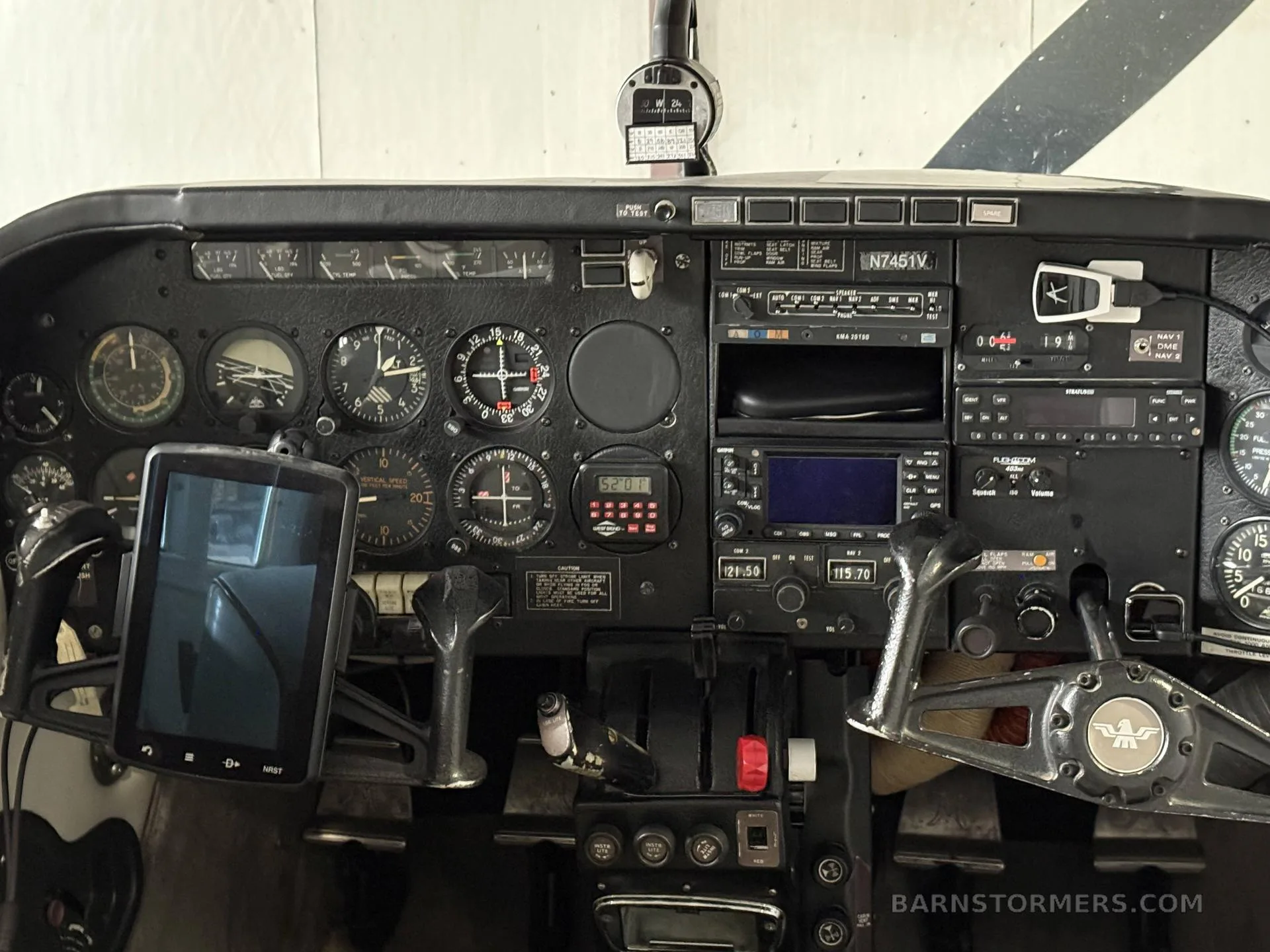 The cockpit of a small aircraft, showing the instrument panel, yokes, and a mounted tablet.