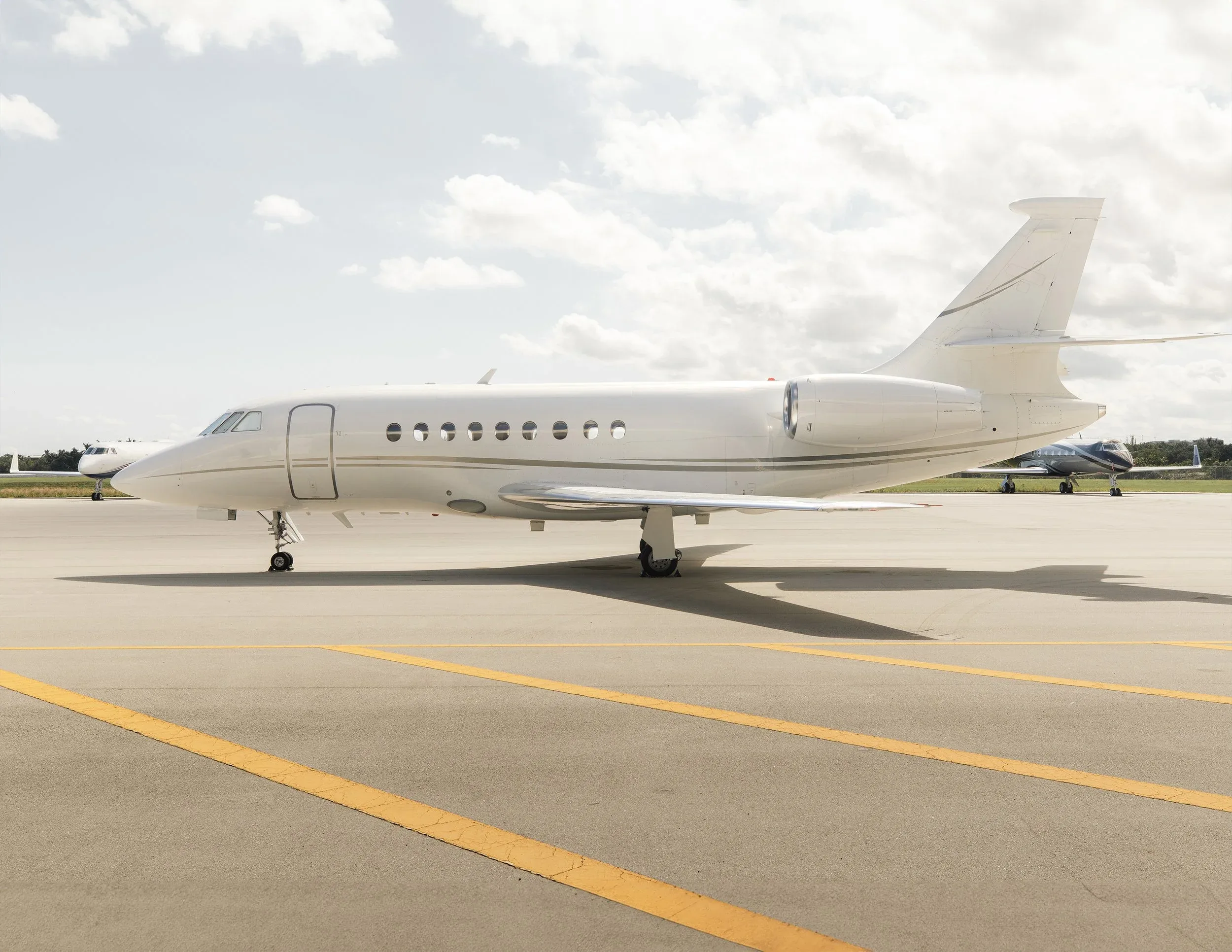 A white business jet, likely a Dassault Falcon, parked on an airport tarmac under a cloudy sky.