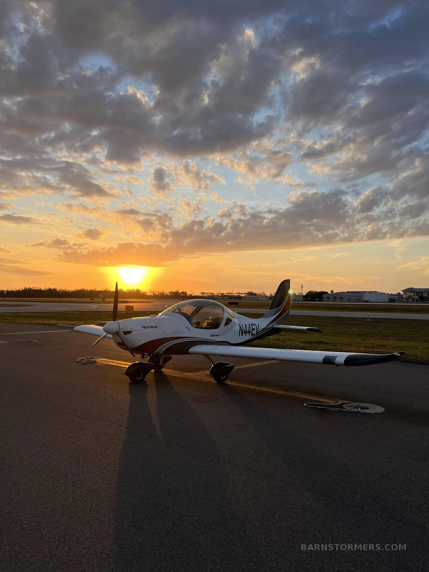 A white and red SportStar aircraft, tail number N44EV, parked on an airfield at sunset.