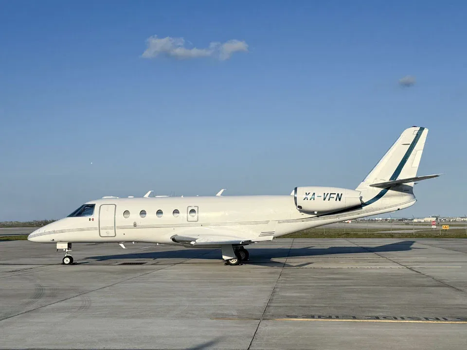 A white business jet with green stripes on the tail, registration XA-VFN, viewed from the side on an airport tarmac.