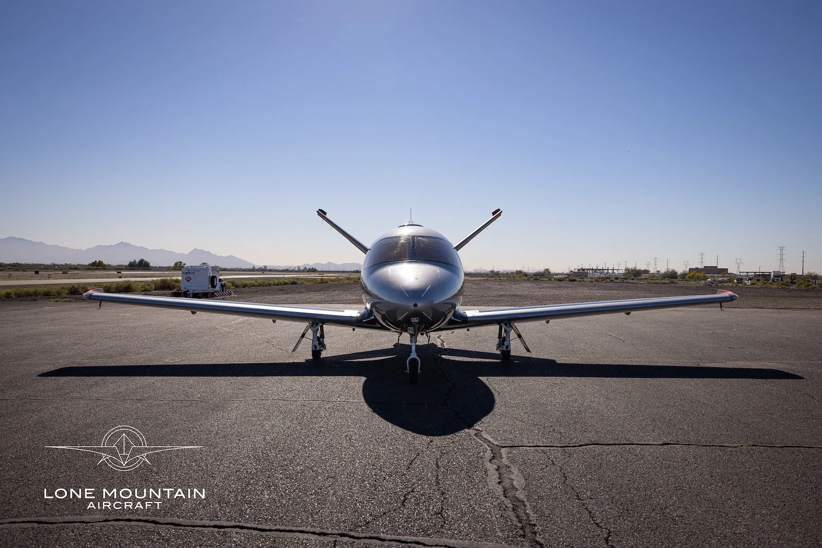 A head-on view of a silver Cirrus Vision Jet (SF50) with its wings extended, parked on an asphalt tarmac.