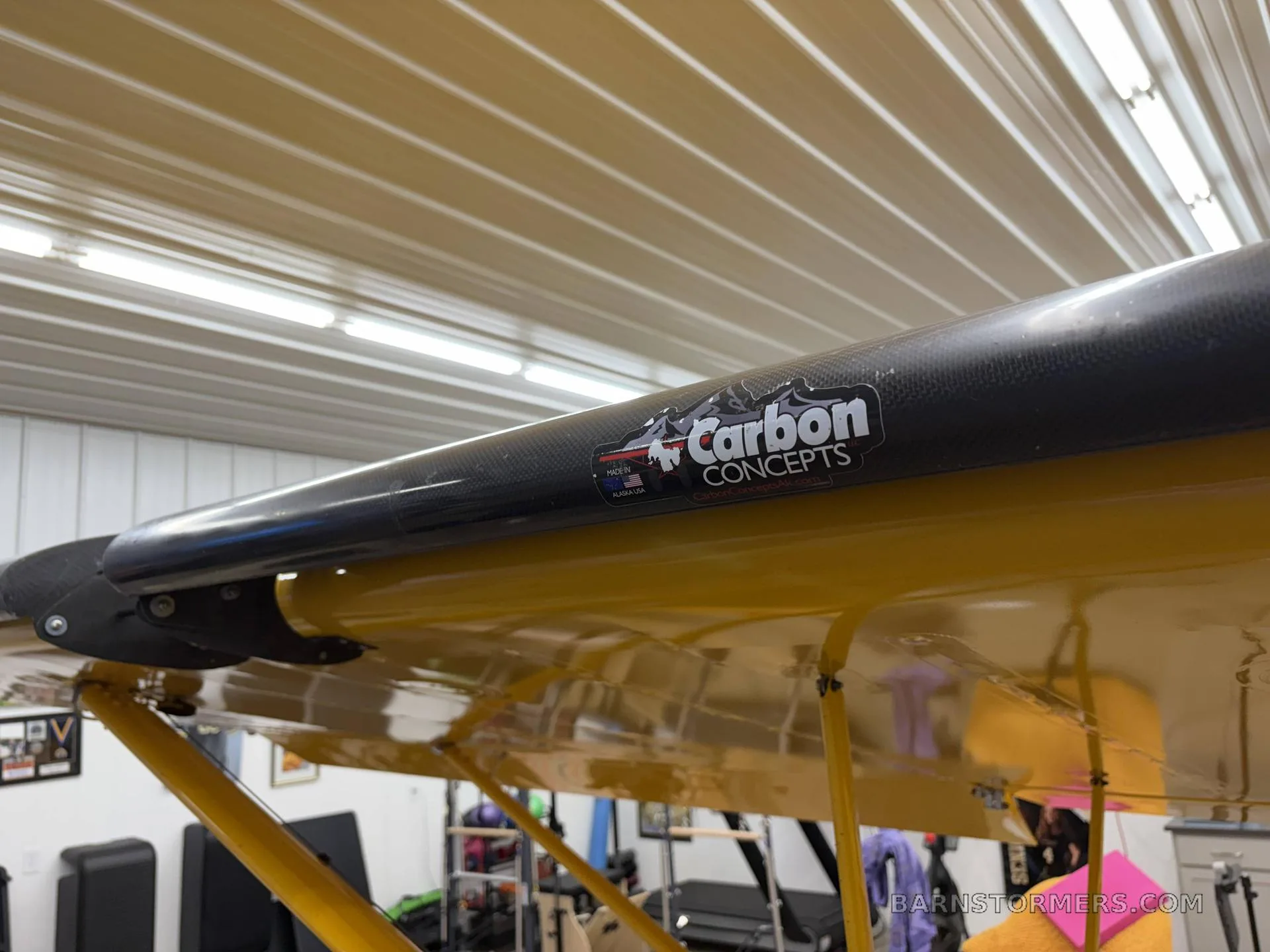 A close-up view of a yellow aircraft wing strut with a "Carbon Concepts" sticker on it.