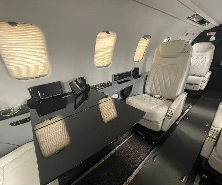 The luxurious interior cabin of a private jet with white quilted seats and a dark glossy table.