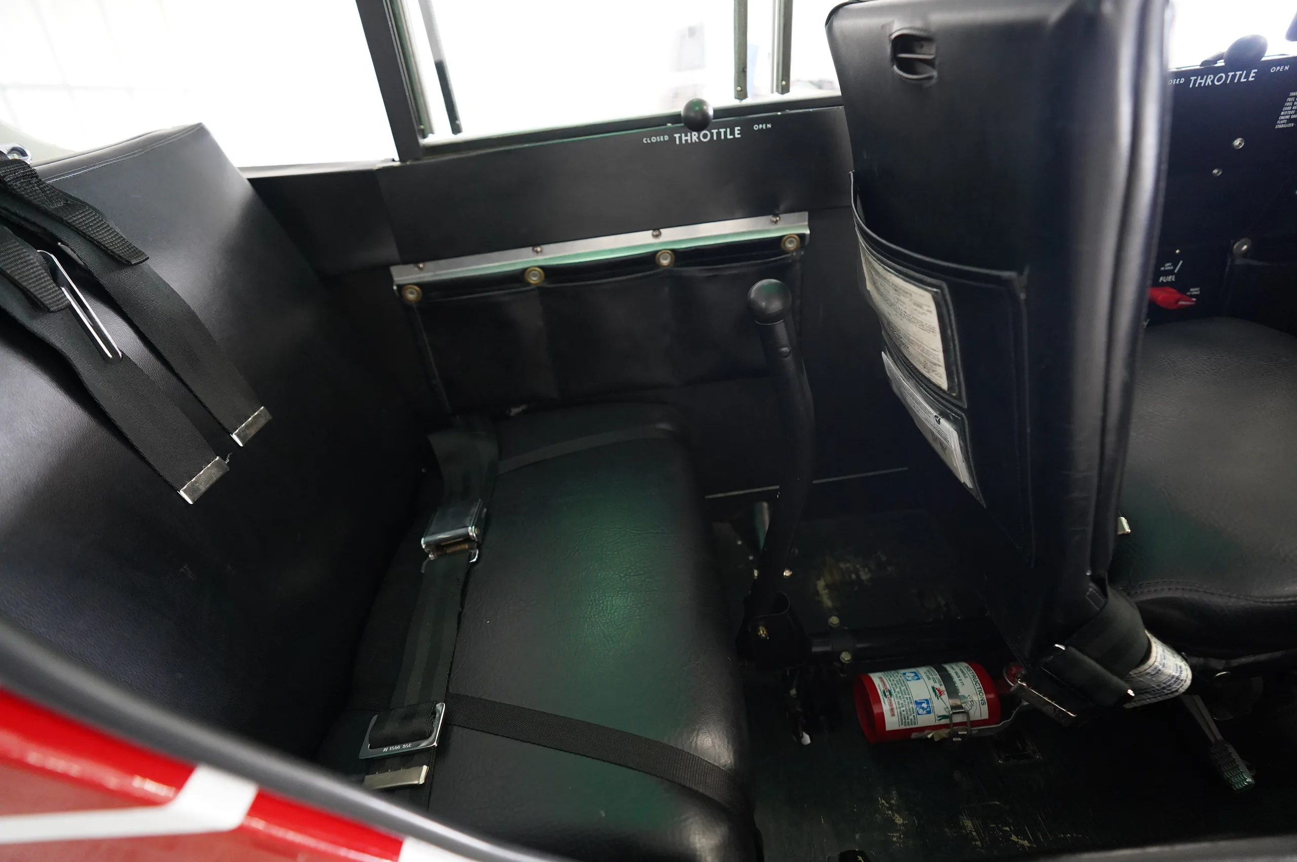 The black upholstered interior cabin of a Piper Cub aircraft, showing seats and a fire extinguisher.