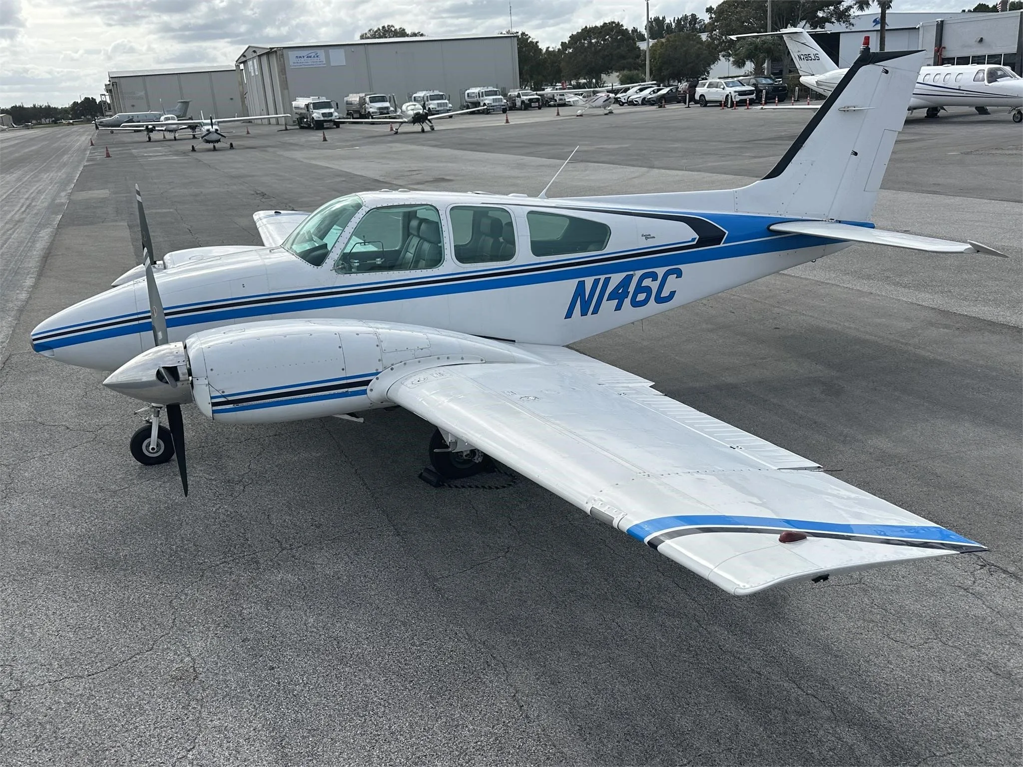 A white and blue twin-engine aircraft, N146C, parked on an airport tarmac with hangars in the background.