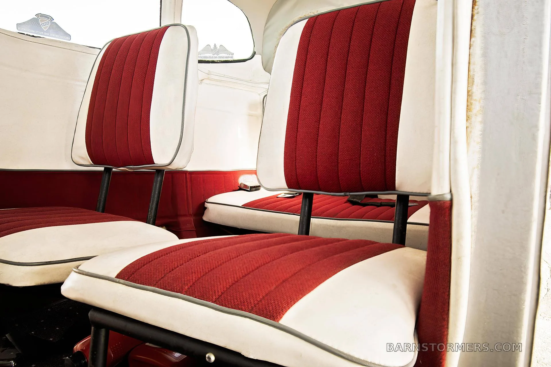 The interior cabin of a small aircraft with red and white upholstered seats.