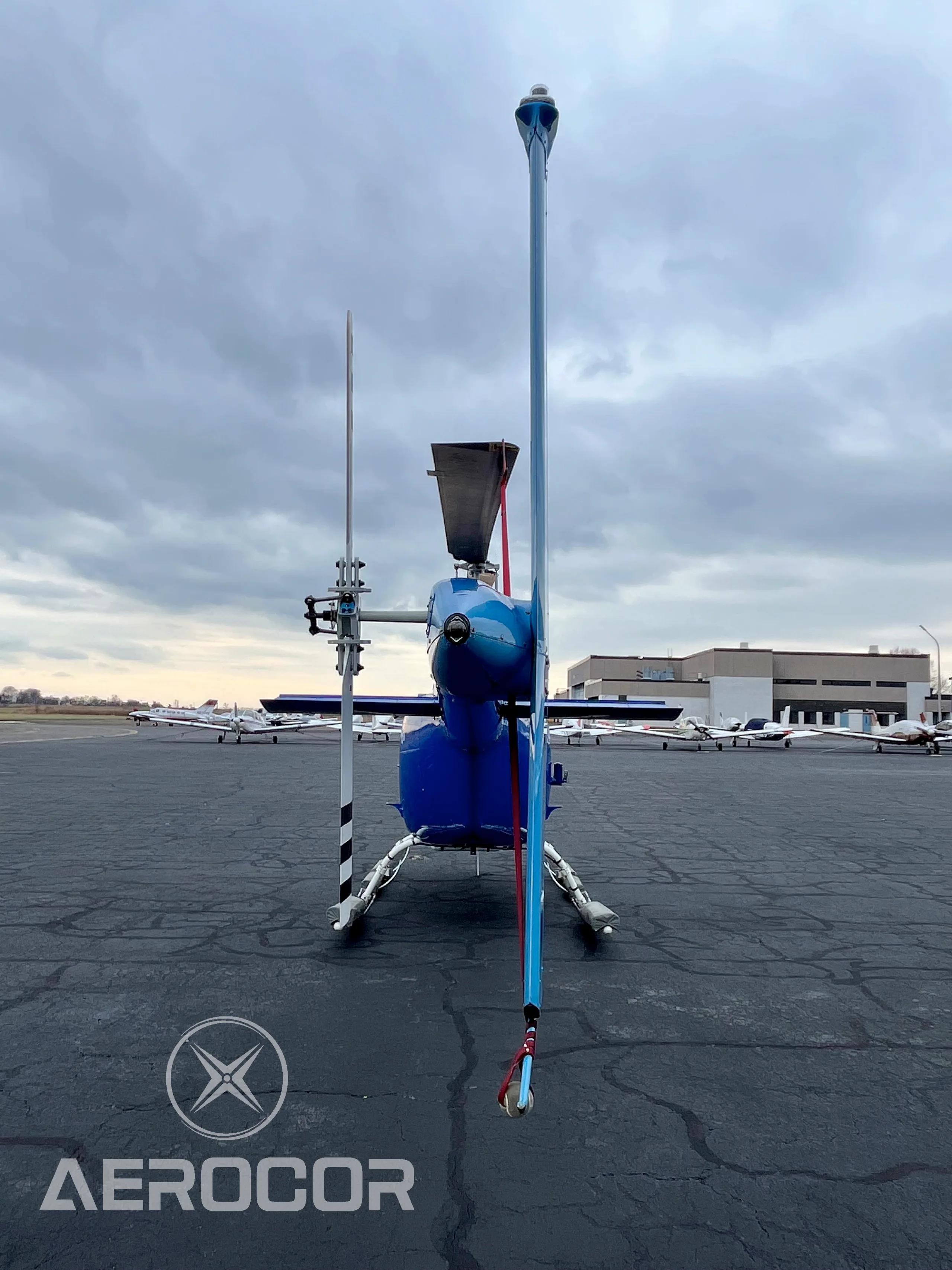 A rear view of the blue and white Bell JetRanger III helicopter, tail number N411DD, showing the tail rotor and vertical stabilizer on an airfield.