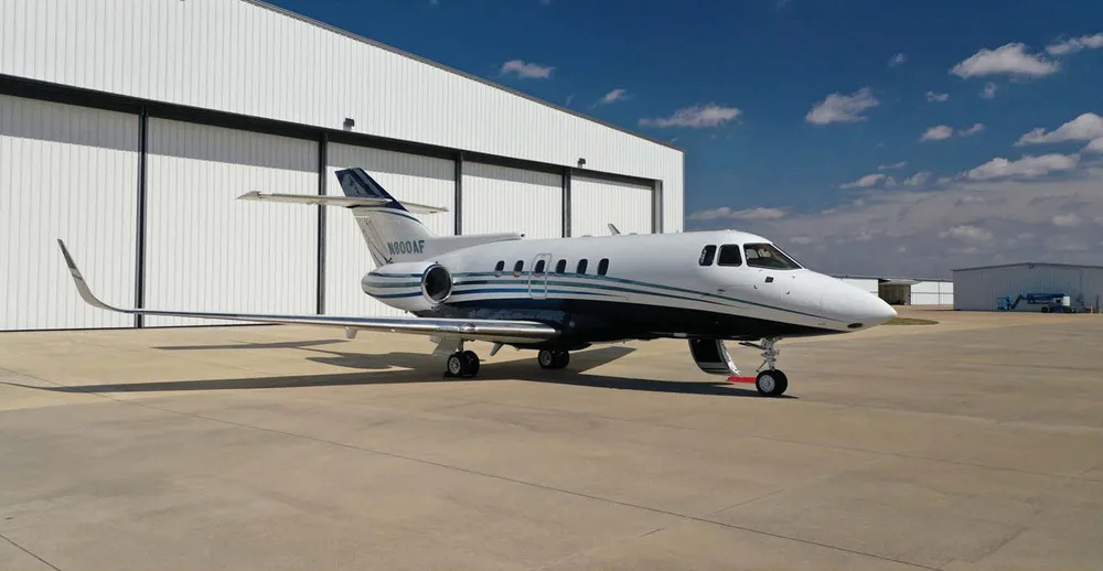 A white and blue Hawker 800XP business jet, registration N800AF, parked on an airfield with a large white hangar in the background.