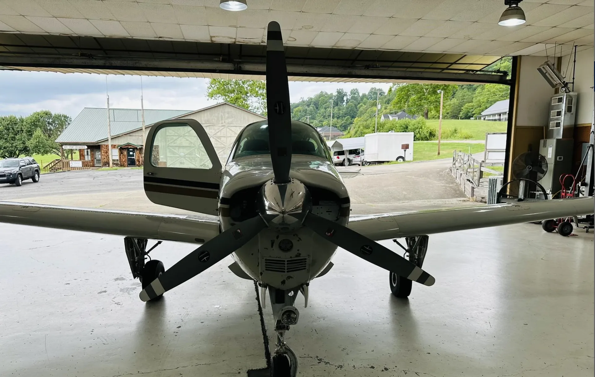 A white and gold Beechcraft Bonanza N7SP with an open door, viewed head-on from inside a hangar.