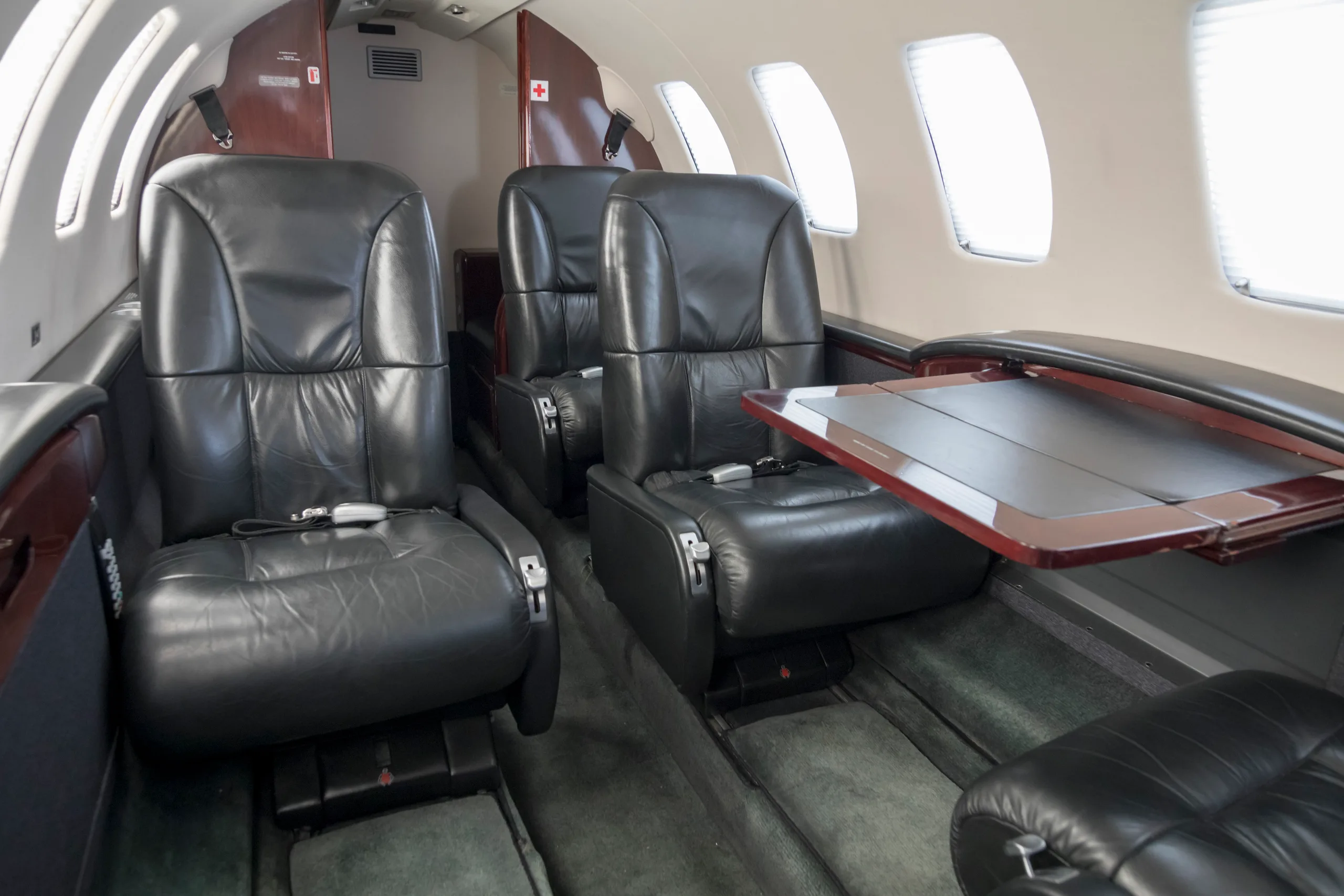 The interior cabin of a private jet with black leather seats and a fold-out table extended on the right side.