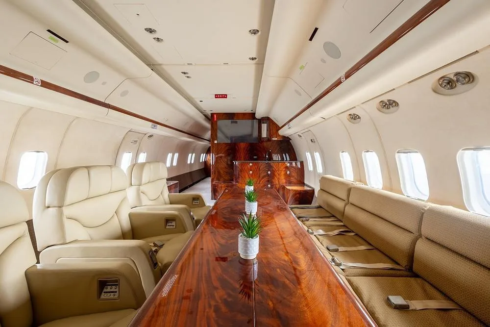 A wide view of a luxurious aircraft cabin with a long wood table and cream seating.