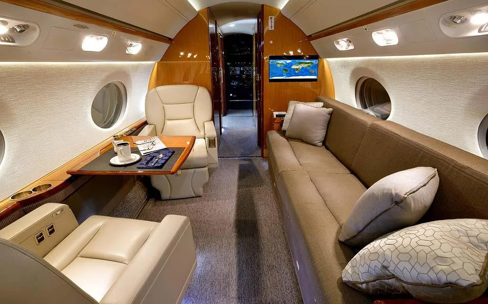 A comfortable private jet cabin interior with a long sofa, a single seat, and a table with a coffee cup.