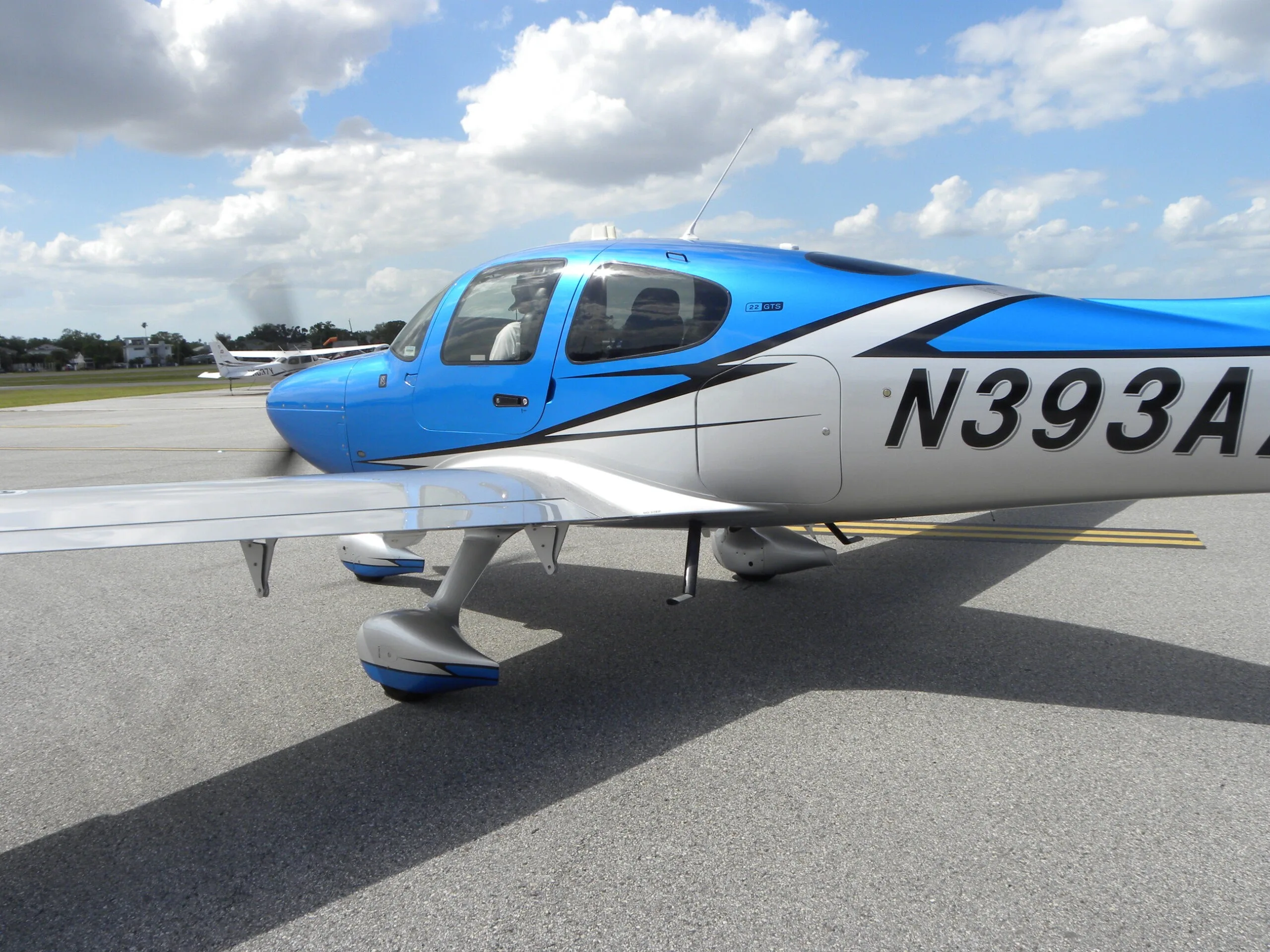 A close-up side view of the cockpit and wing of a blue and silver Cirrus SR22 aircraft with registration N393AA.