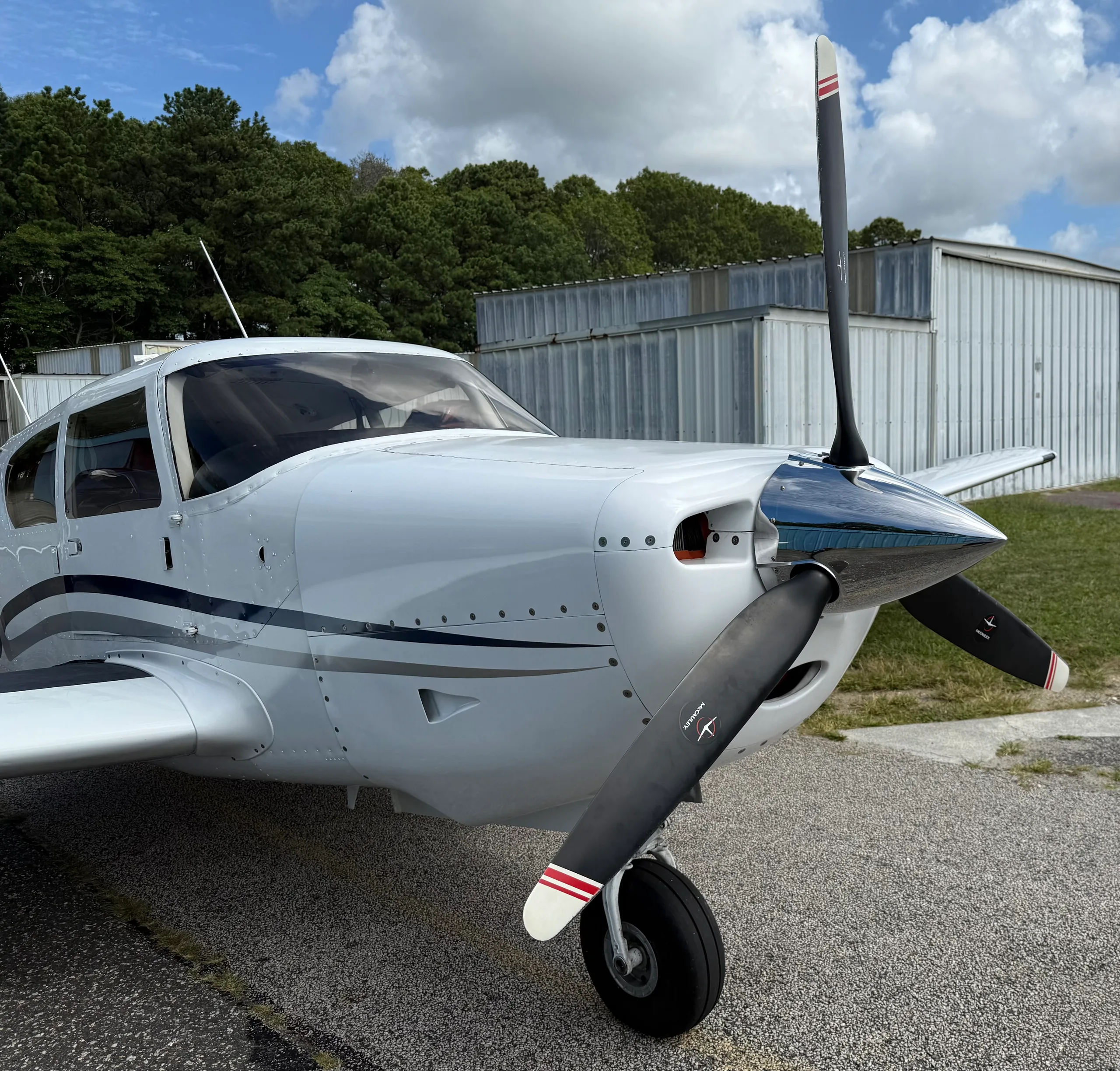 Close-up front view of the propeller and nose of a white single-engine aircraft with blue and gray stripes.