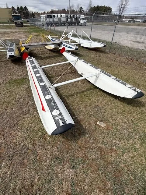 A pair of white aircraft floats with red stripes lying on the grass at an airfield.