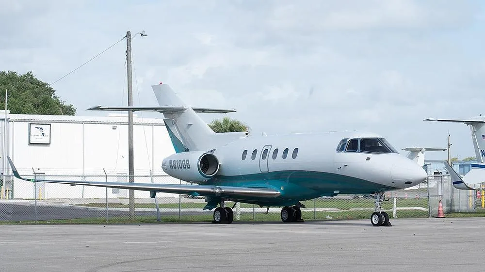 A side view of the N810GB Hawker 800XP business jet with a white and teal paint scheme parked on an airfield.