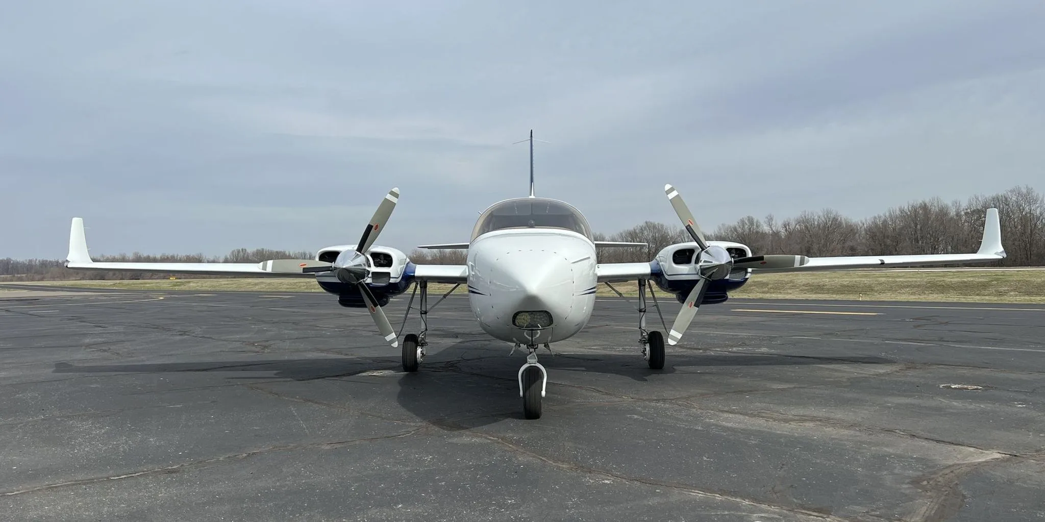 Front view of the white and blue twin-engine aircraft, N25LL, on an asphalt runway.