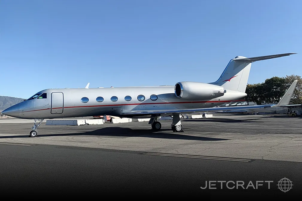 A silver Gulfstream G650 business jet with a red stripe on the tarmac under a clear sky.
